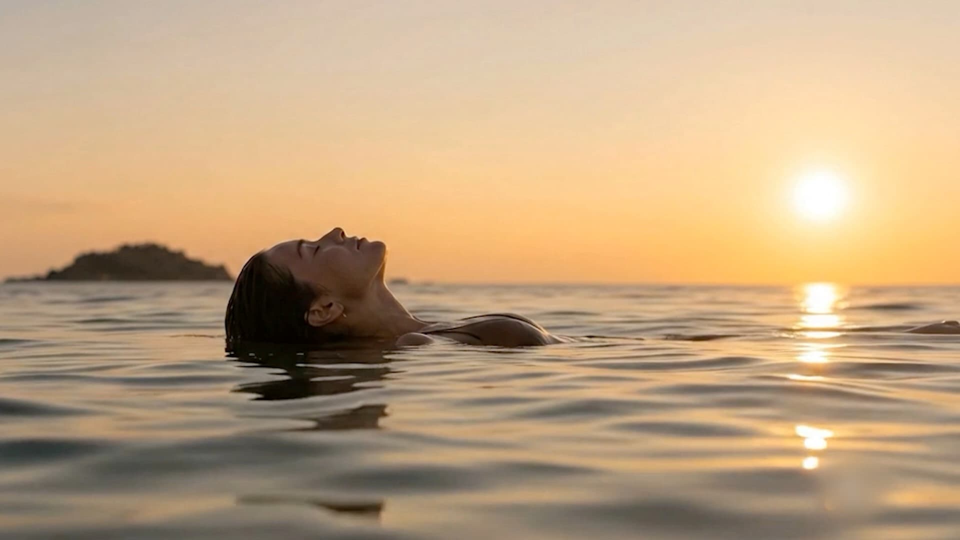 A woman floating on her back in calm water at sunset